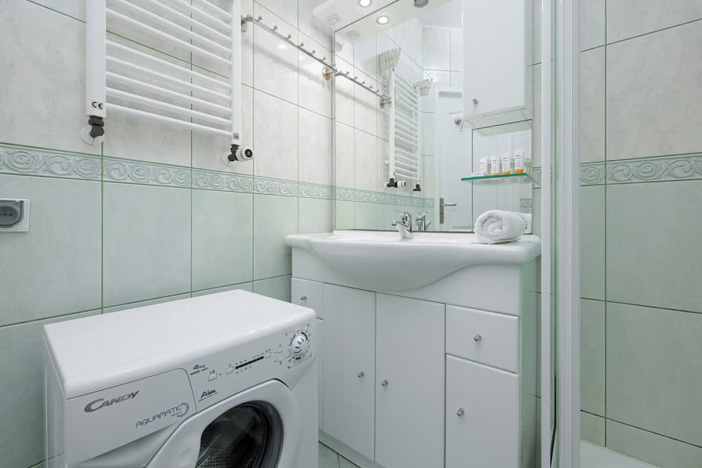 A clean, tiled bathroom featuring a sink, bathtub, and washing machine, ensuring comfort and functionality for longer stays.