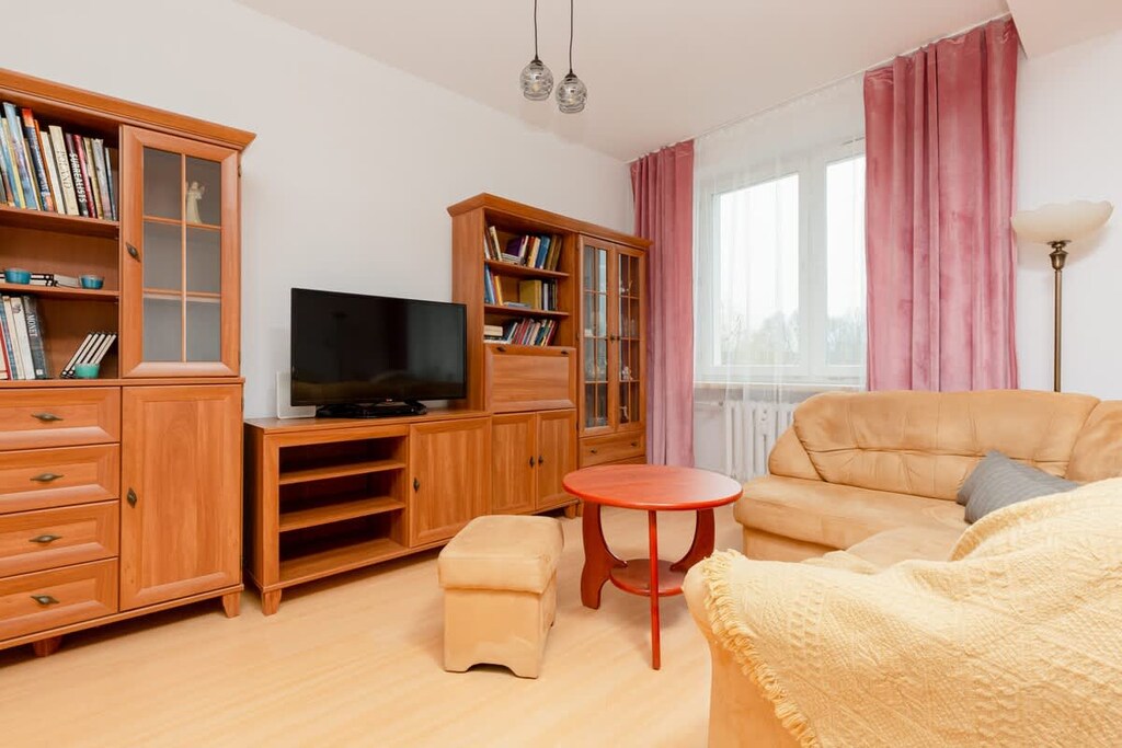  comfortable living area with a wooden entertainment unit, sofa set, and large windows adorned with pink curtains.
