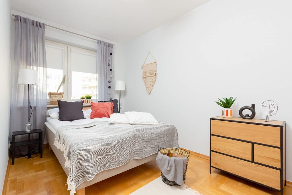 Another bedroom with a wooden bed, neutral-colored linens, and a bedside table. The decor is simple, and the space is well-lit.