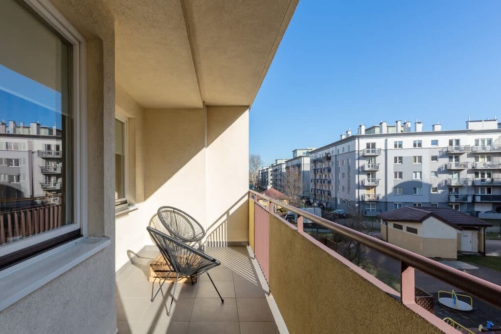 A spacious balcony with a table and chairs, overlooking a modern residential area. The view includes buildings and an open sky.