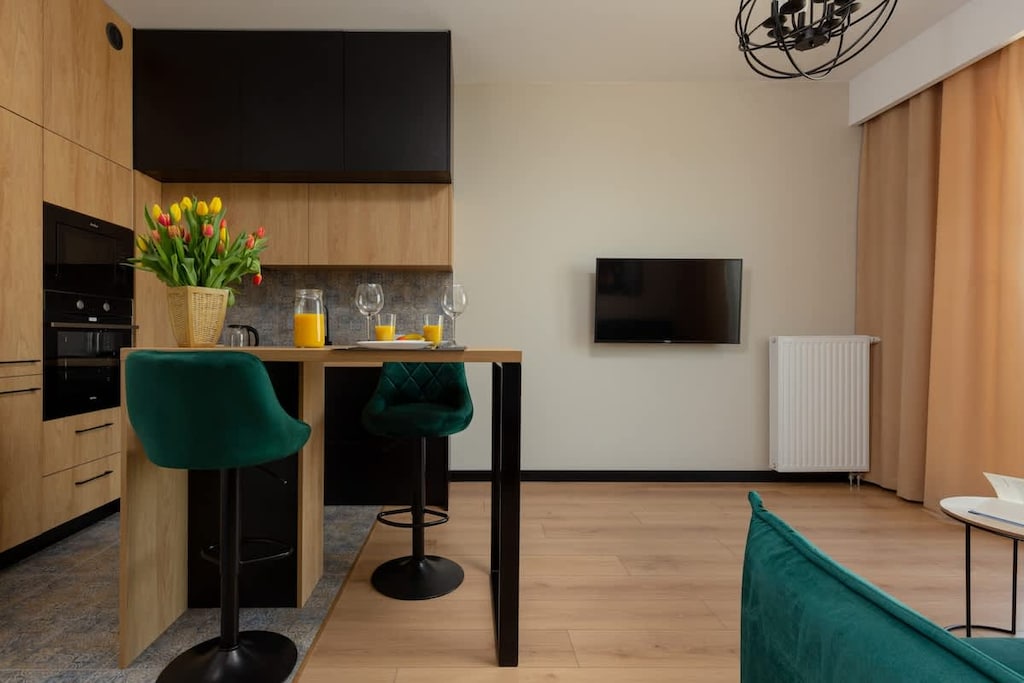Another angle of the living room showcasing a dining area with a wooden table and green chairs, seamlessly blending with the open kitchen space.
