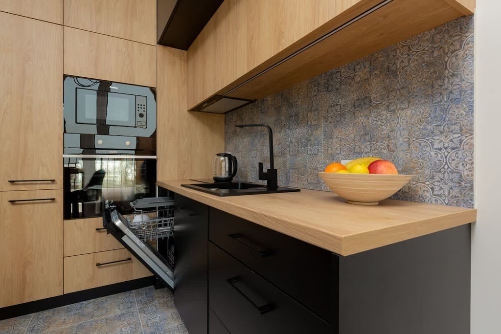 A compact kitchen with wooden cabinets, a modern backsplash, and a well-organized countertop complete with fresh fruits.