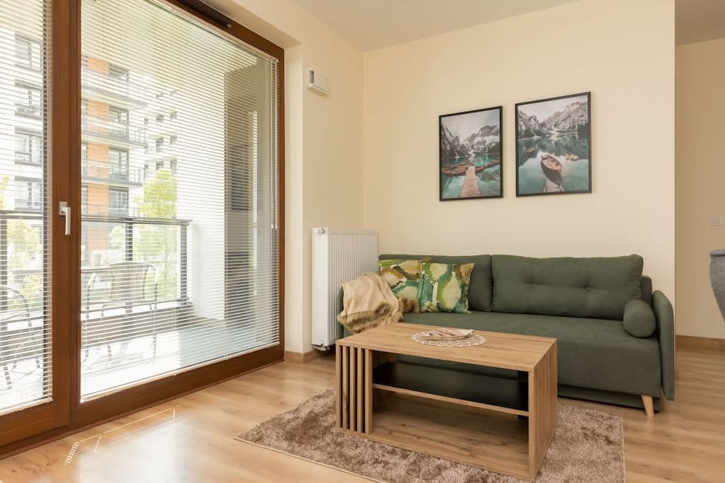 A cozy living room with a comfortable green sofa, a coffee table, and large windows providing natural light.

