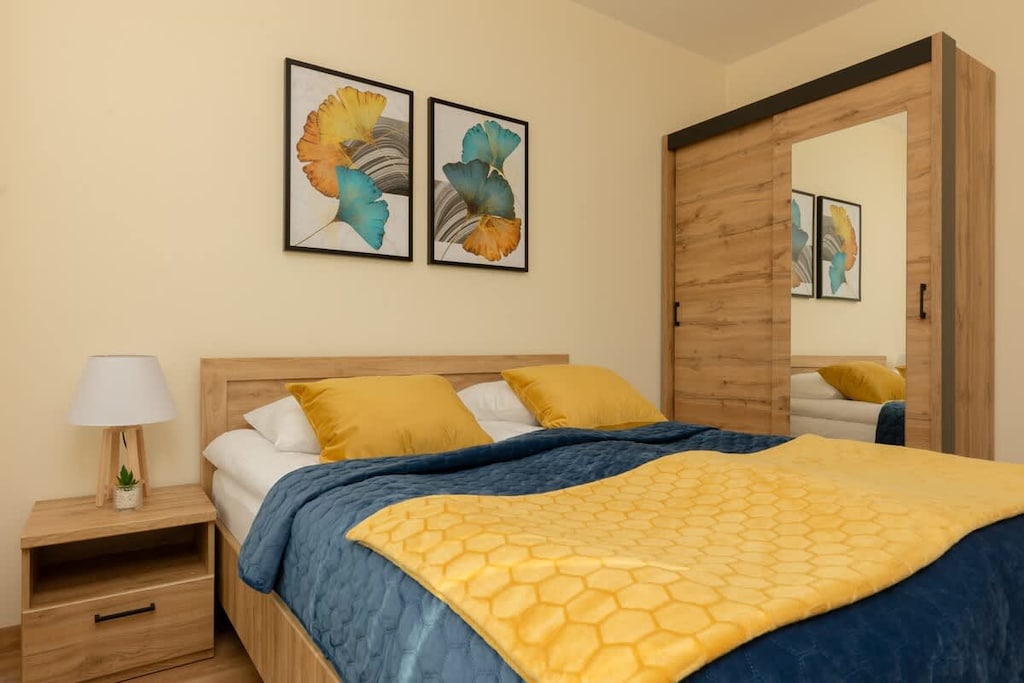 A bright bedroom with a double bed, yellow accents, and a spacious wardrobe.
