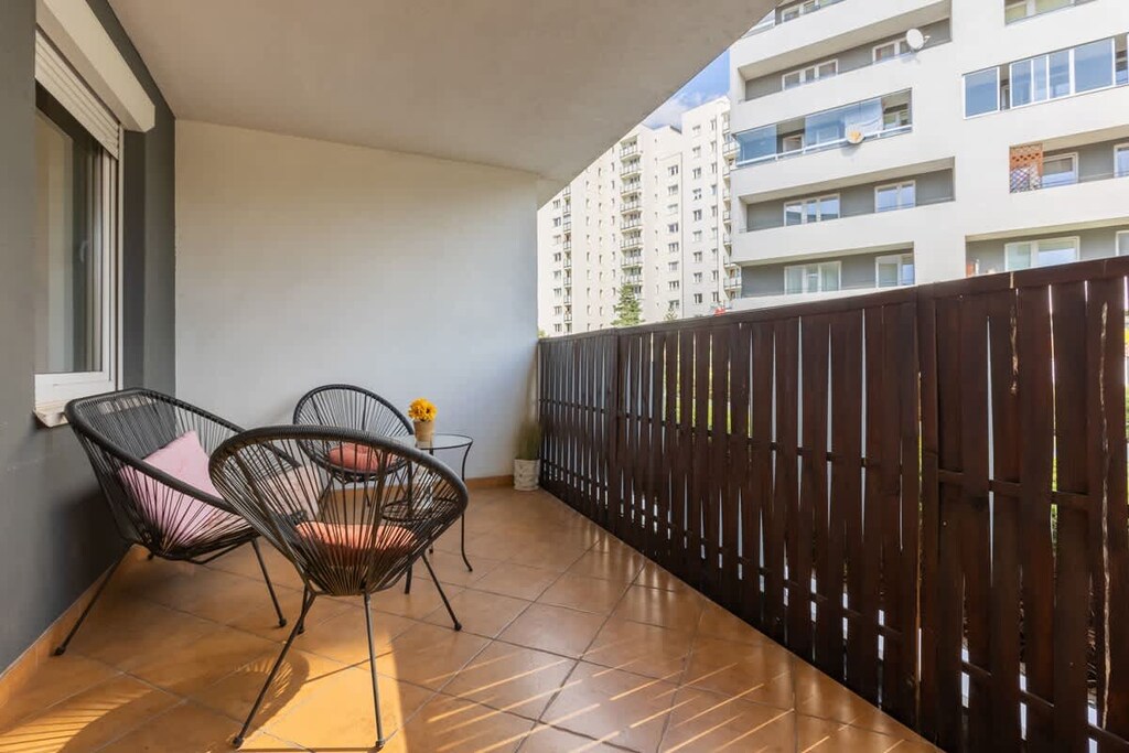A balcony with wooden flooring, black chairs, and a view of nearby residential buildings, perfect for enjoying the outdoors.

