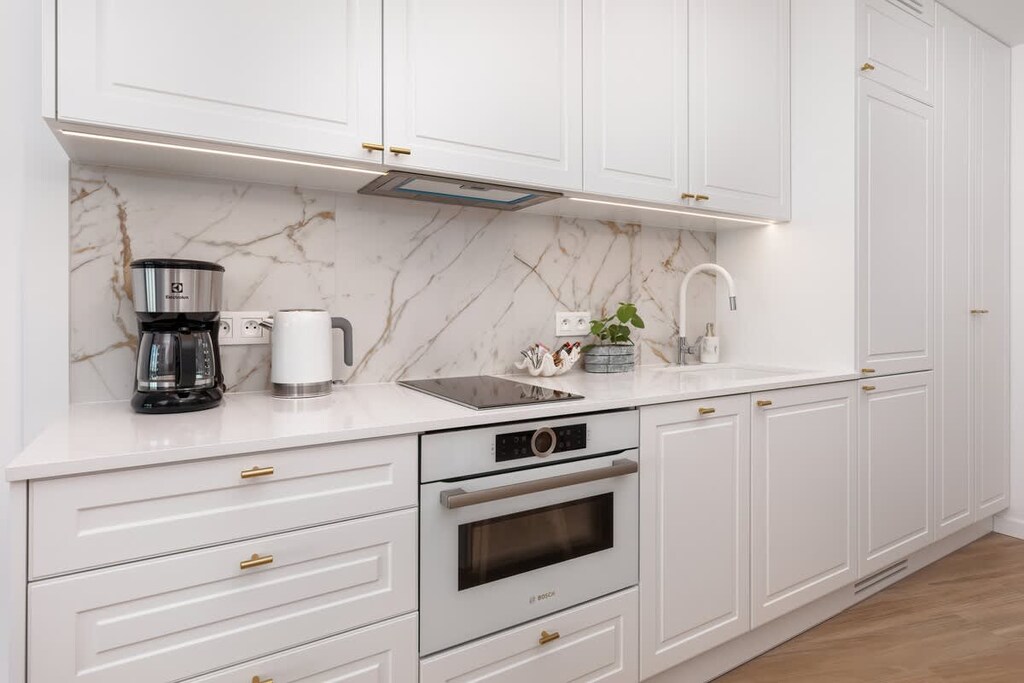 A stylish white kitchen with marble countertops, built-in appliances, and thoughtful decor, blending elegance and functionality.

