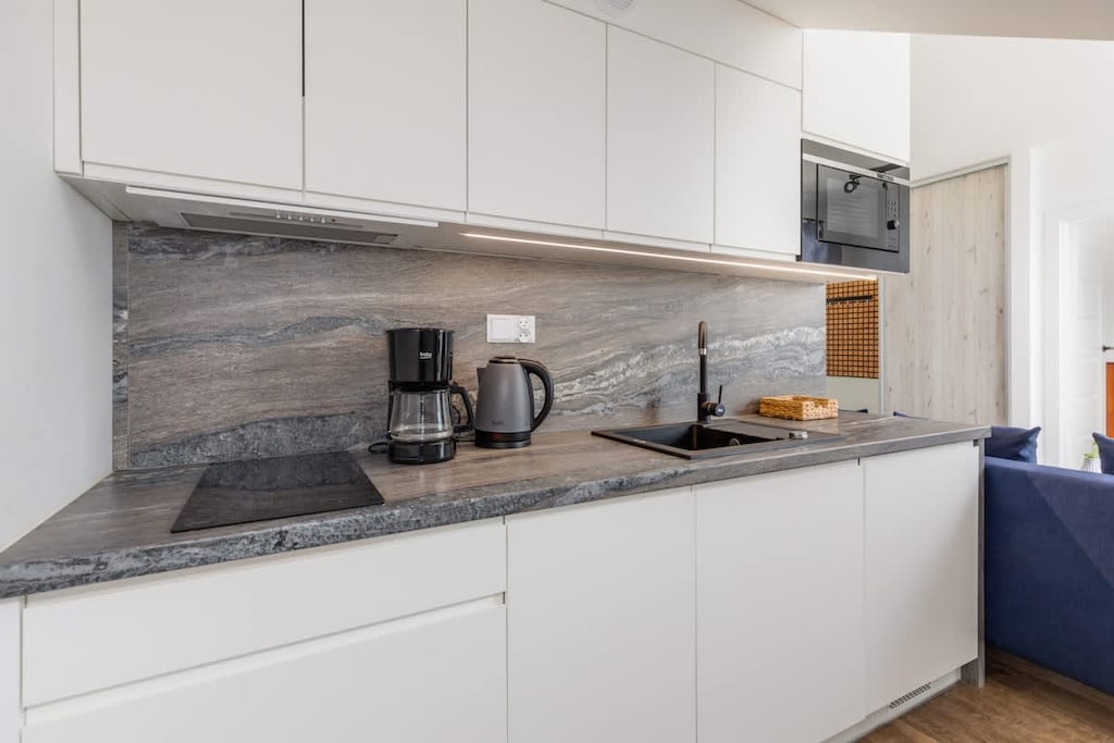 A sleek kitchen corner with white cabinets, gray stone backsplash, and built-in appliances, blending style and functionality.
