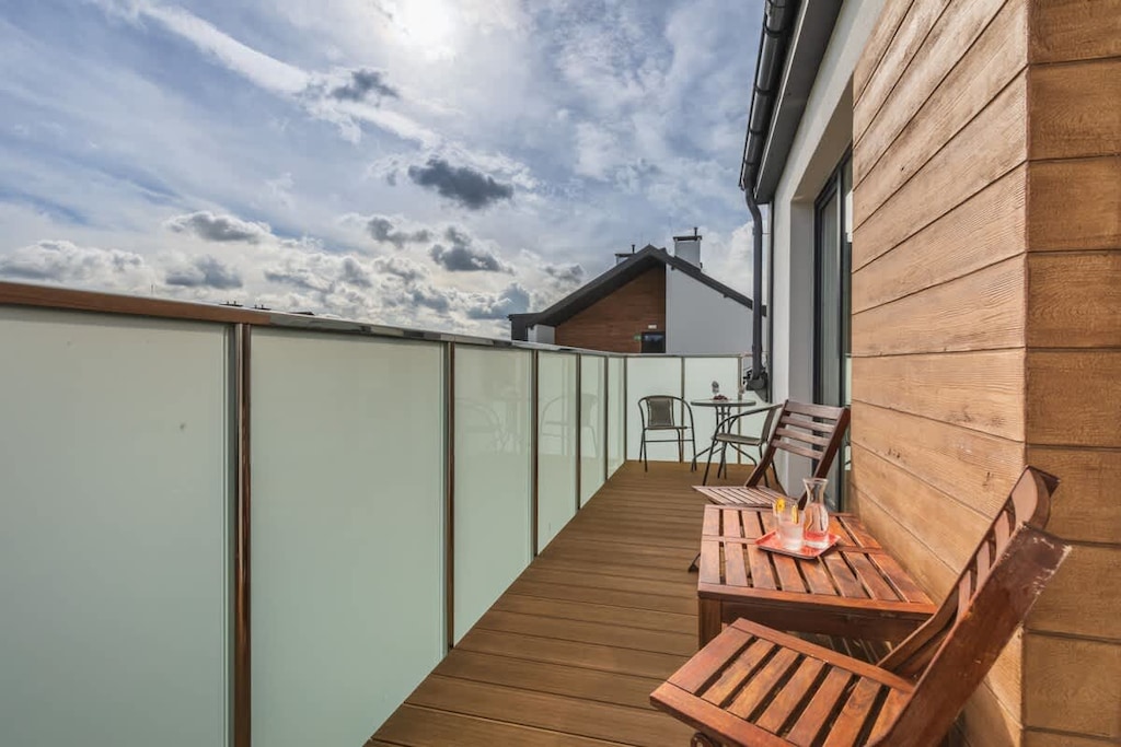 A balcony with wooden flooring, a small table, and chairs, offering a relaxing outdoor space with a view.
