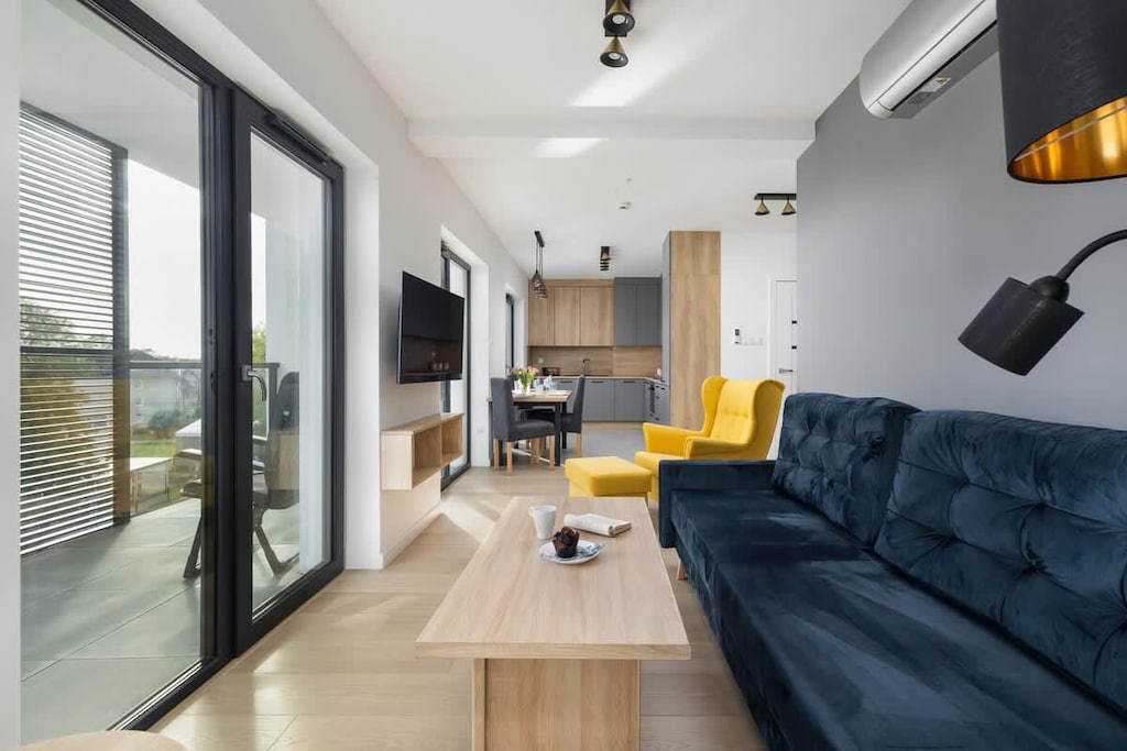 A modern living room with a blue sofa, a yellow armchair, and a bright open-plan design featuring large windows.
