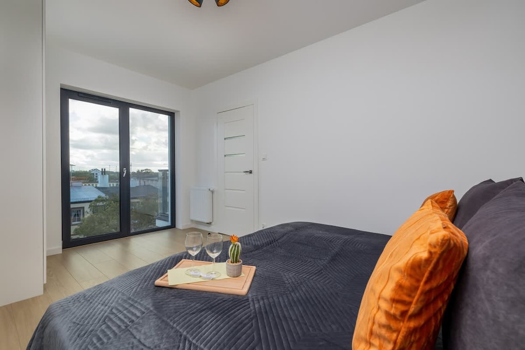 A cozy bedroom with a grey bedspread, decorative orange cushions, and a clean, minimalistic aesthetic.
