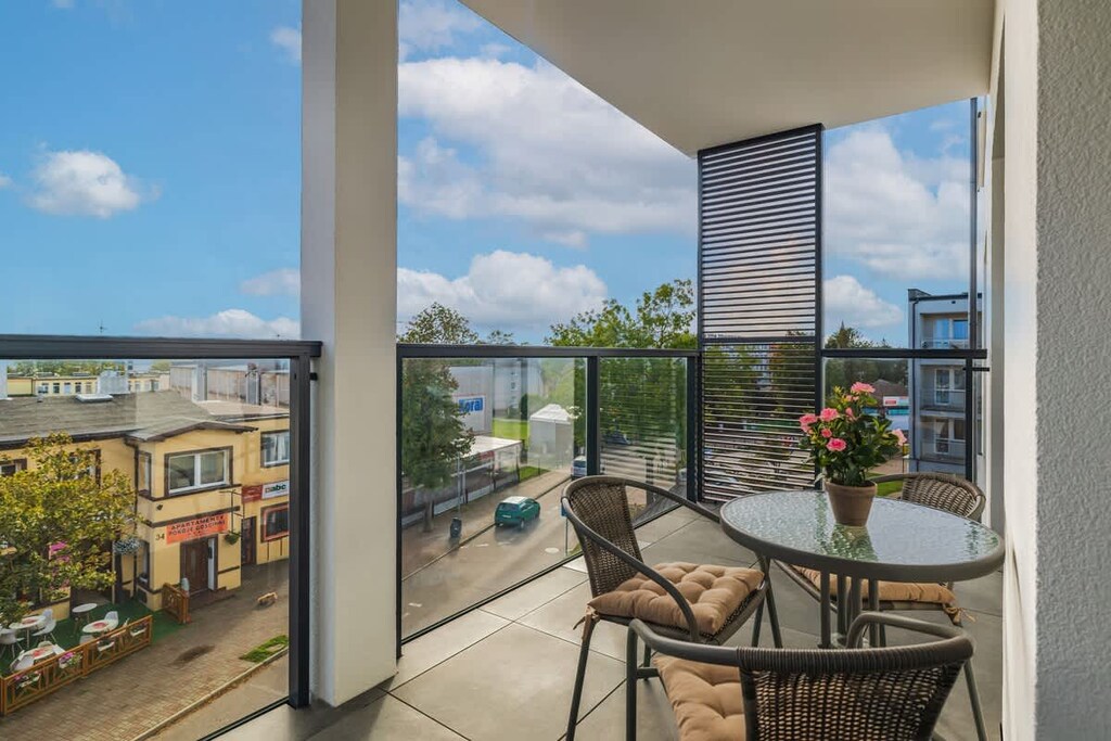 A spacious balcony with a small table, wicker chairs, and a scenic view of the surrounding area.
