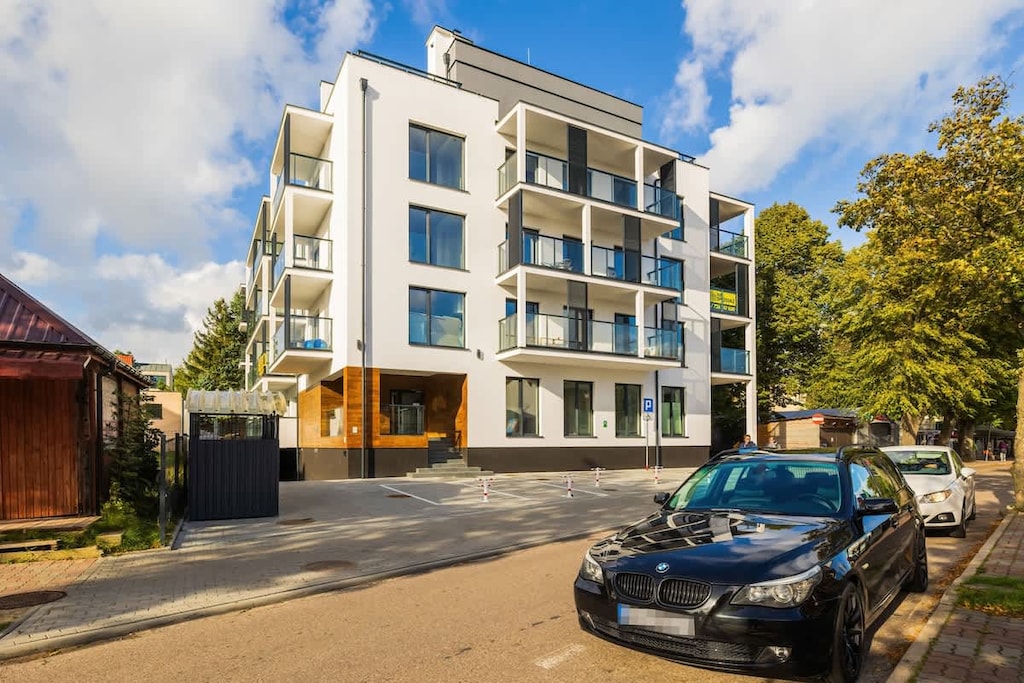 The exterior of a modern residential building with clean lines, large windows, and a landscaped entrance.
