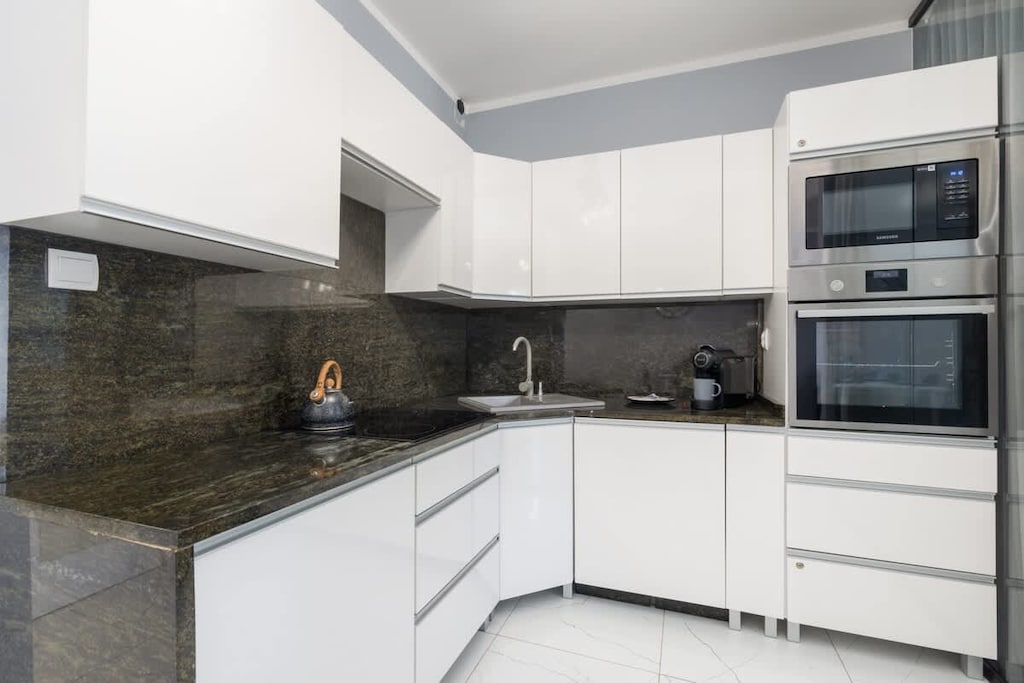 A sleek white kitchen with black countertops and integrated appliances.
