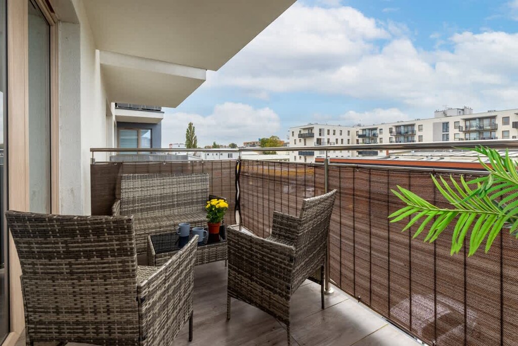 A balcony with wicker chairs, a table, and a view of the residential area.
