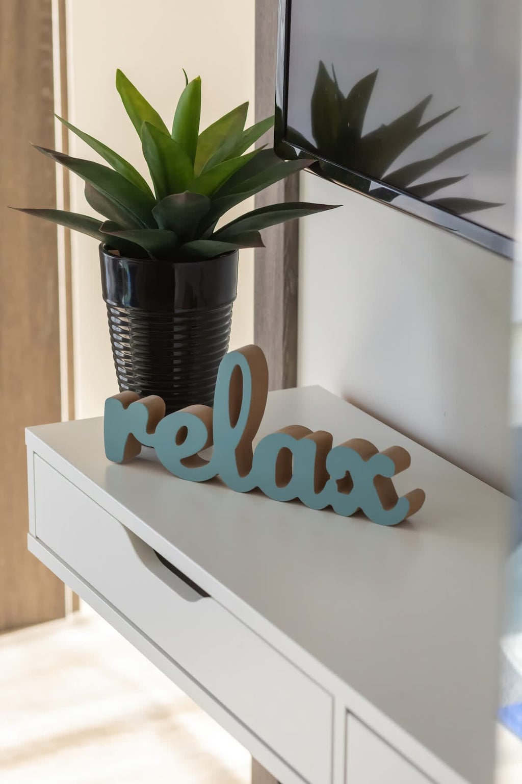 A decorative "Relax" sign with a small plant on a white shelf.

