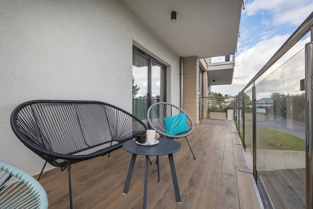 A balcony with rattan chairs and a glass railing overlooking a scenic view.

