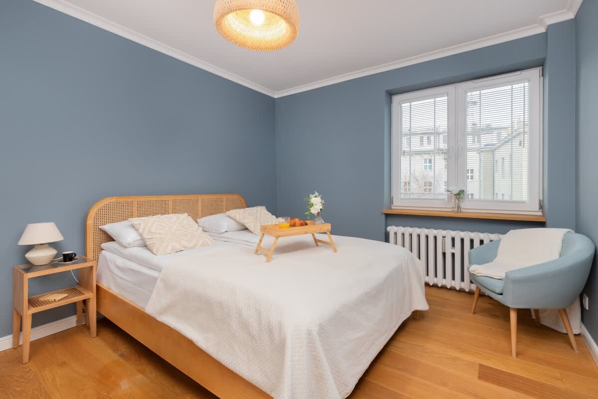 Spacious bedroom with a comfortable double bed, blue accent wall, and ample natural light from the windows.