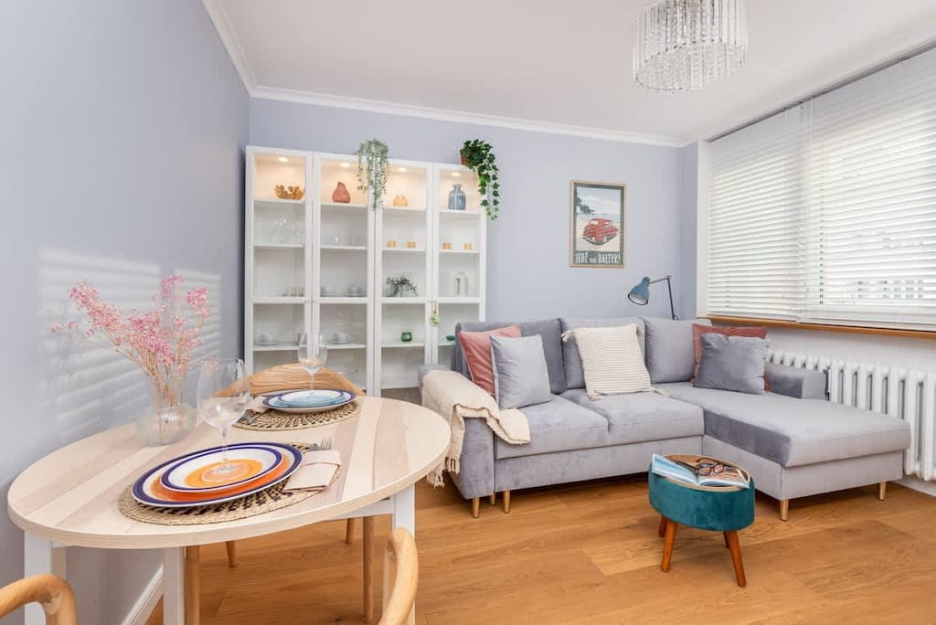 Another view of the living room showing a larger sofa, shelves, and a dining area with tableware set on the table.