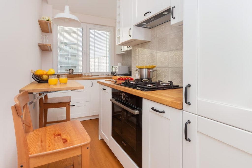 Compact kitchen with modern appliances, including a stove, oven, and cabinets in a light color scheme.