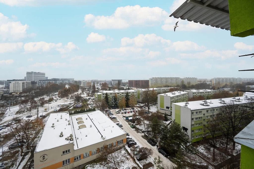 A balcony view overlooking a snow-covered residential area with surrounding apartment buildings and a clear blue sky.

