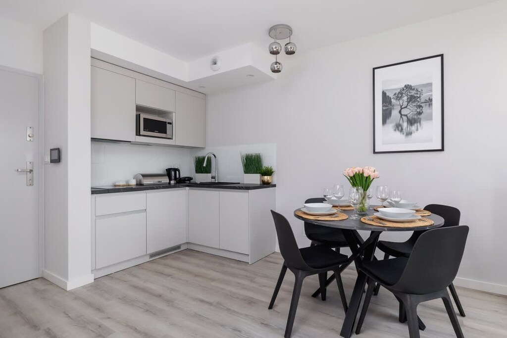 A bright open-plan dining and kitchen area with a minimalist design, white walls, and black furniture for a sleek contrast.

