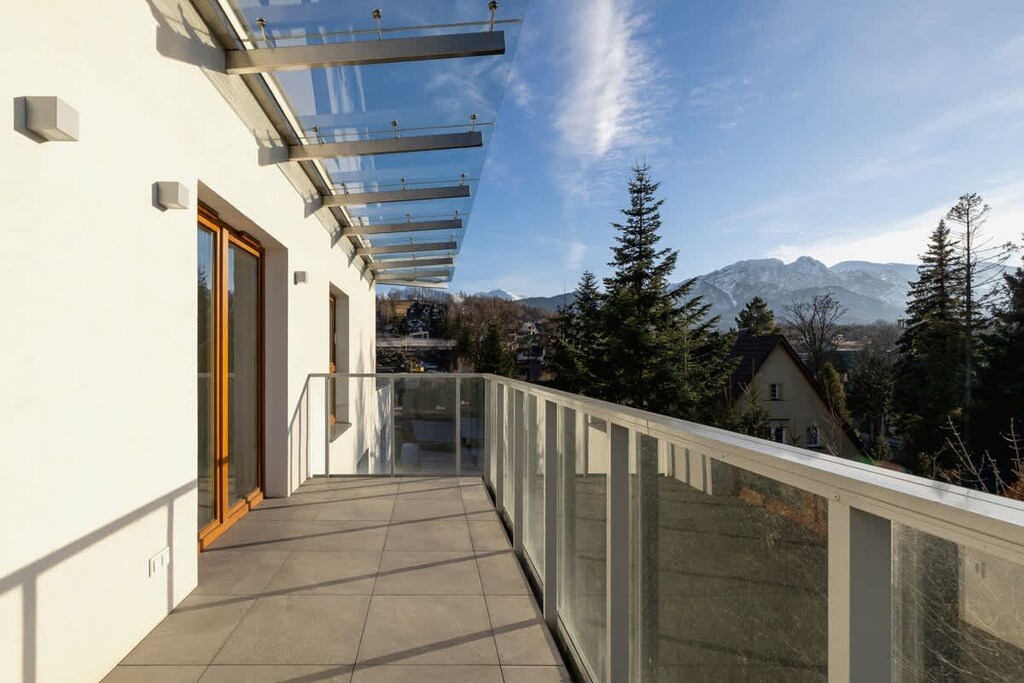 A spacious balcony with a glass railing and stunning views of a forested mountain landscape, offering a perfect place to relax.

