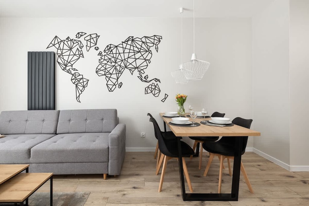 A stylish living and dining area featuring a gray sofa, a wooden dining table, and a world map wall decoration adding a modern touch.

