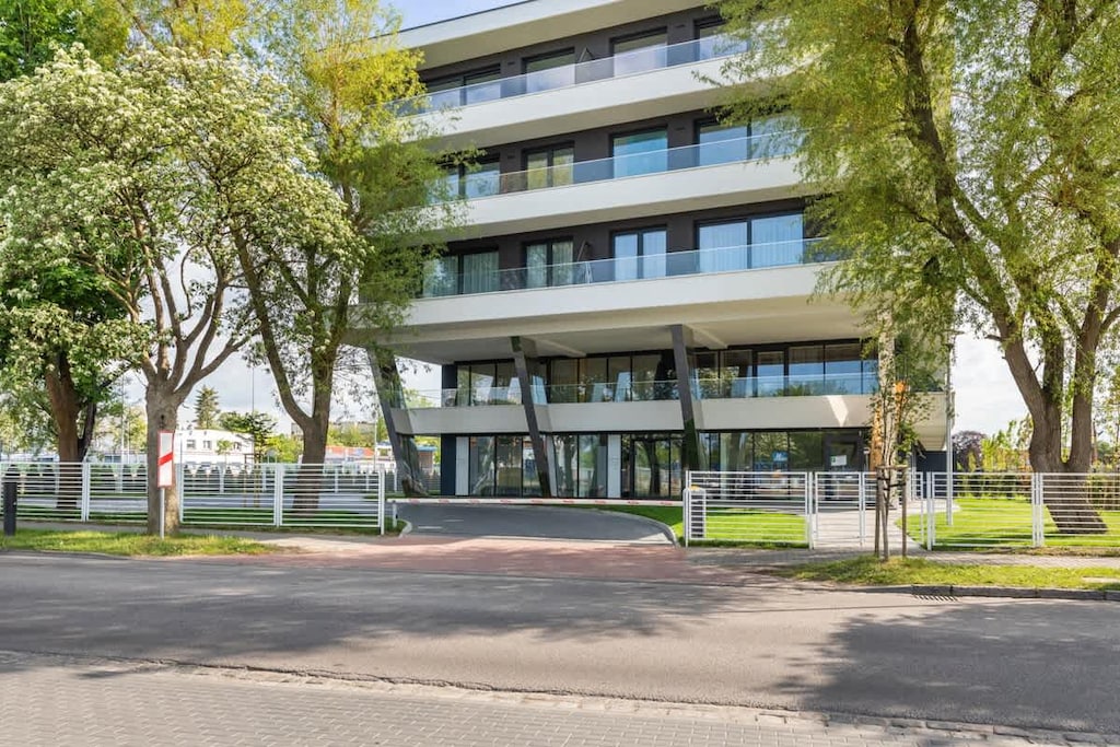 An exterior view of a modern residential building, surrounded by trees and featuring large glass windows for a bright and open look.

