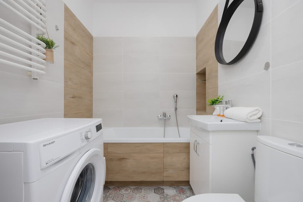 A modern bathroom with a washing machine, white sink, and circular mirror mounted above.


