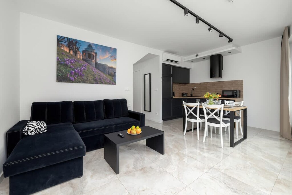 A cozy living room featuring a dark sofa, wall art, and a stylish dining table in the corner.

