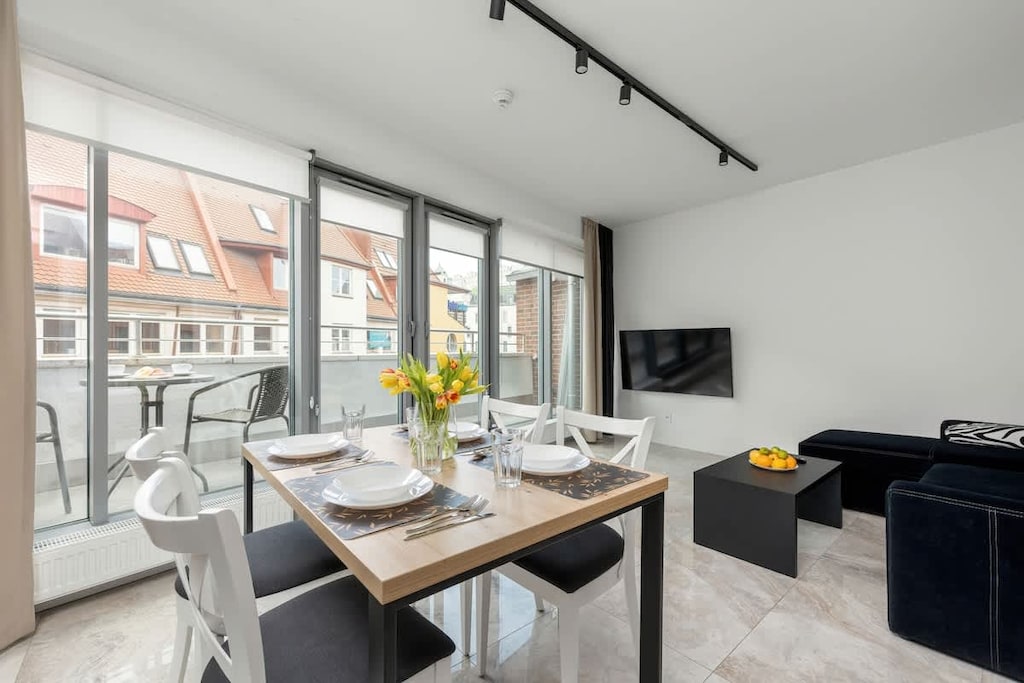 A bright dining area with a round table set for four, surrounded by large windows letting in natural light.

