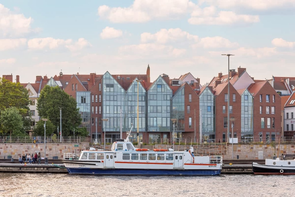 A waterfront view with a boat cruising by, lined with colorful buildings and reflections in the water.

