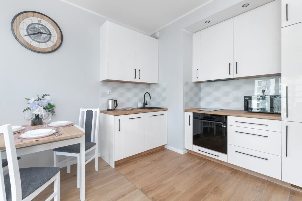 A stylish white kitchen with built-in appliances and wooden flooring. A small dining table is ideal for meals or work.