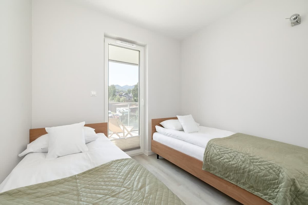 A bright bedroom with a double bed covered in green bedding. Neutral tones and simple decor create a calming atmosphere.