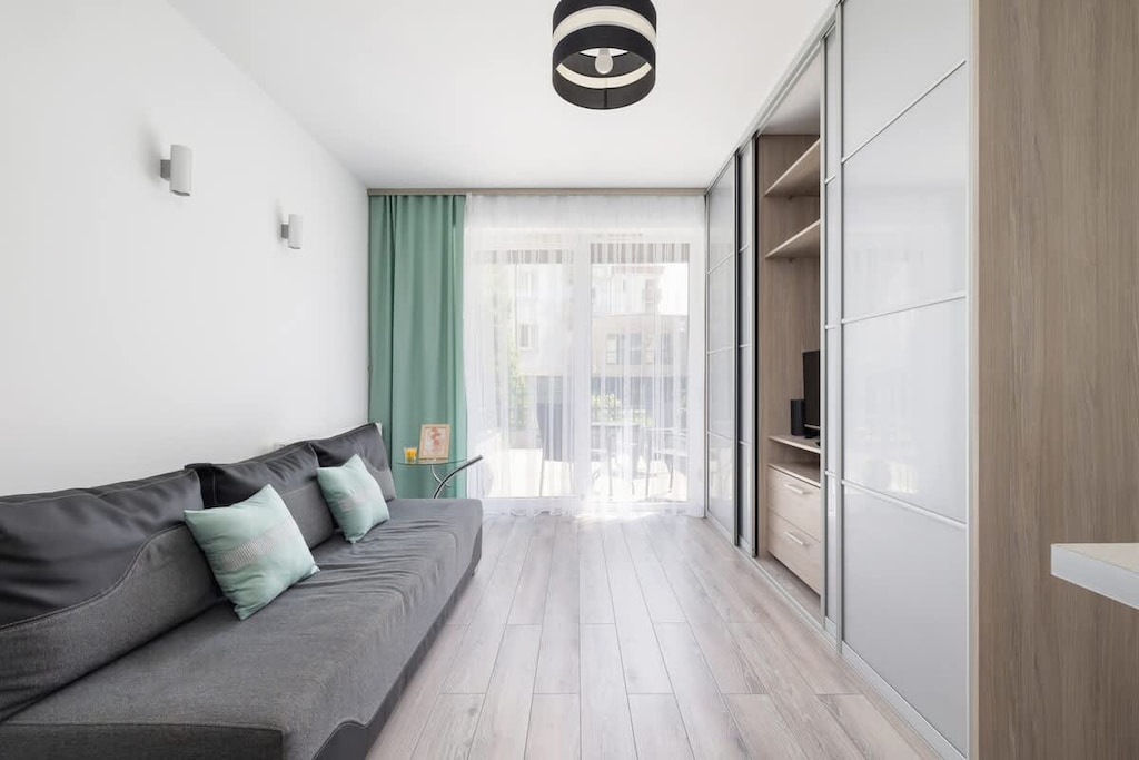 Modern living room with a large window, green curtains, grey sofa, and light wooden flooring.