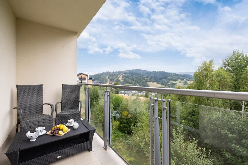 A charming balcony includes comfortable seating and a scenic view over rolling hills and greenery – perfect for enjoying morning coffee or sunset drinks.