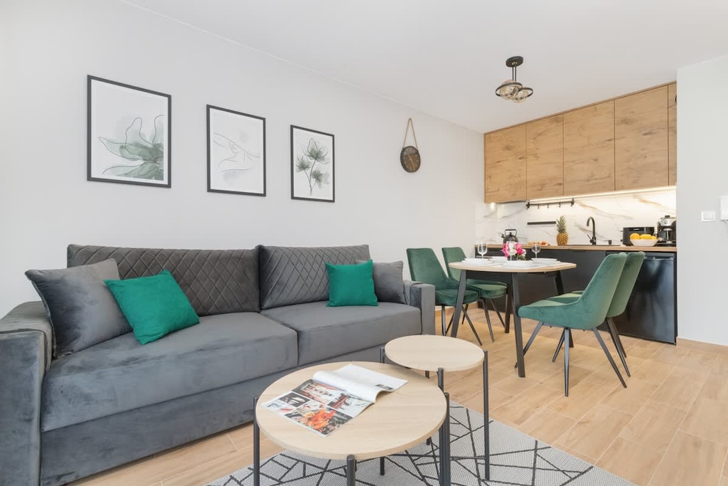 A stylish living room featuring a gray sofa, round dining table, and soft wall decor. The room is bright and welcoming with modern furnishings.