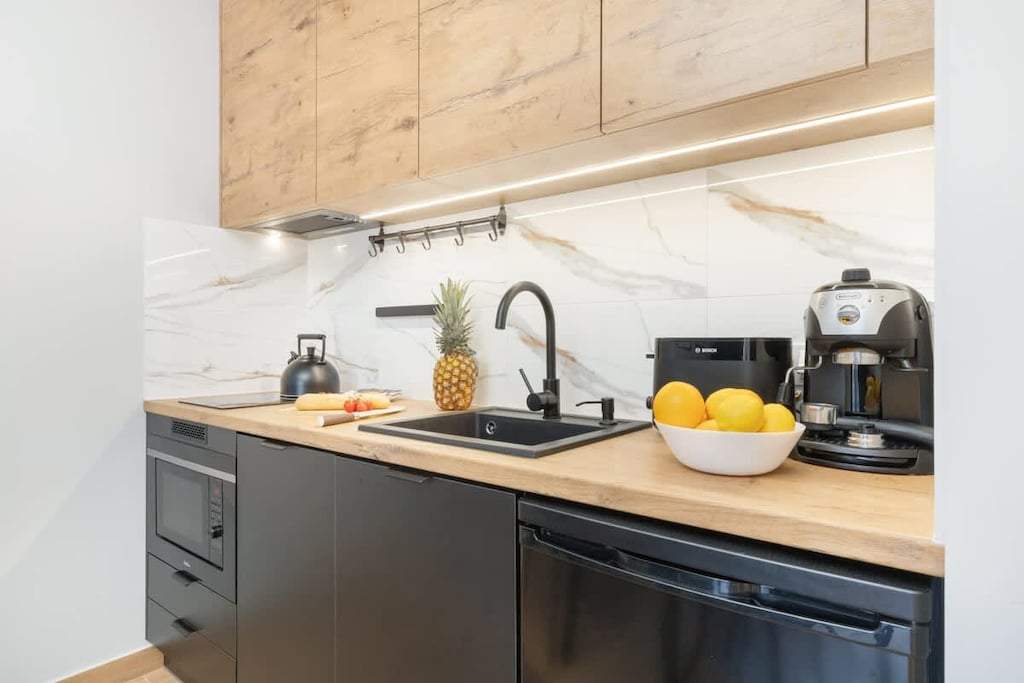 A sleek kitchen with wood cabinets and a black countertop. A kettle and fruit bowl add functionality and charm.