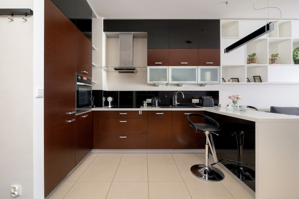 A compact kitchen with bar stools, dark cabinetry, and a tiled backsplash in neutral tones.