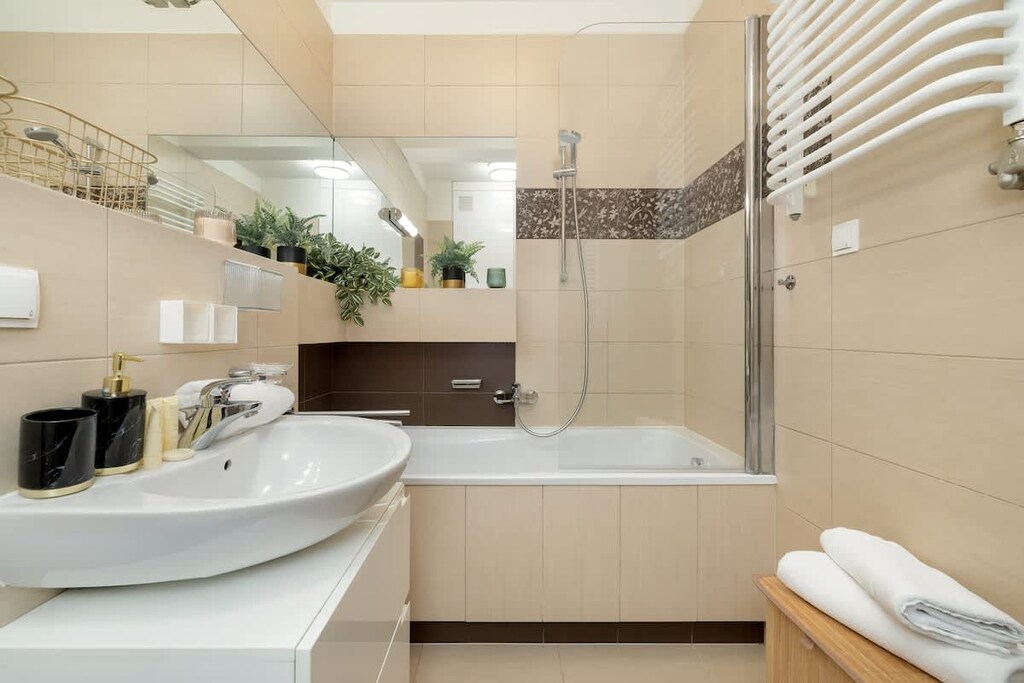 A clean bathroom with beige tiles, a bathtub, and rolled white towels neatly arranged on the side.