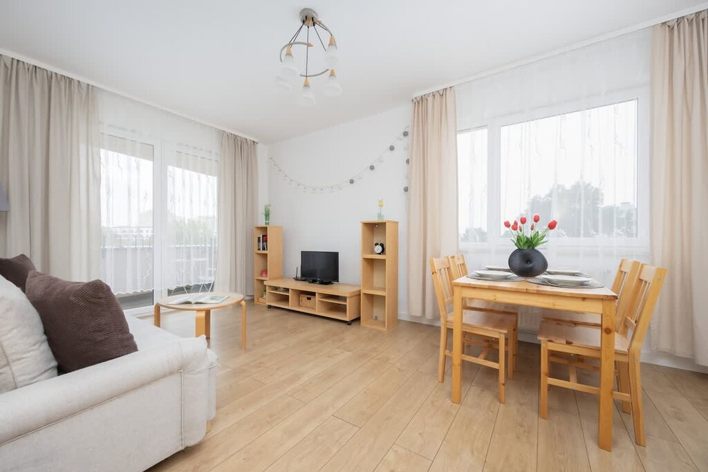 A spacious living and dining area with a beige sofa, wooden furniture, and large windows that brighten the room.