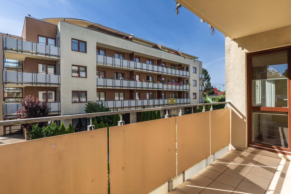 A spacious balcony with a view of a residential complex, offering ample outdoor space and privacy with a beige railing.