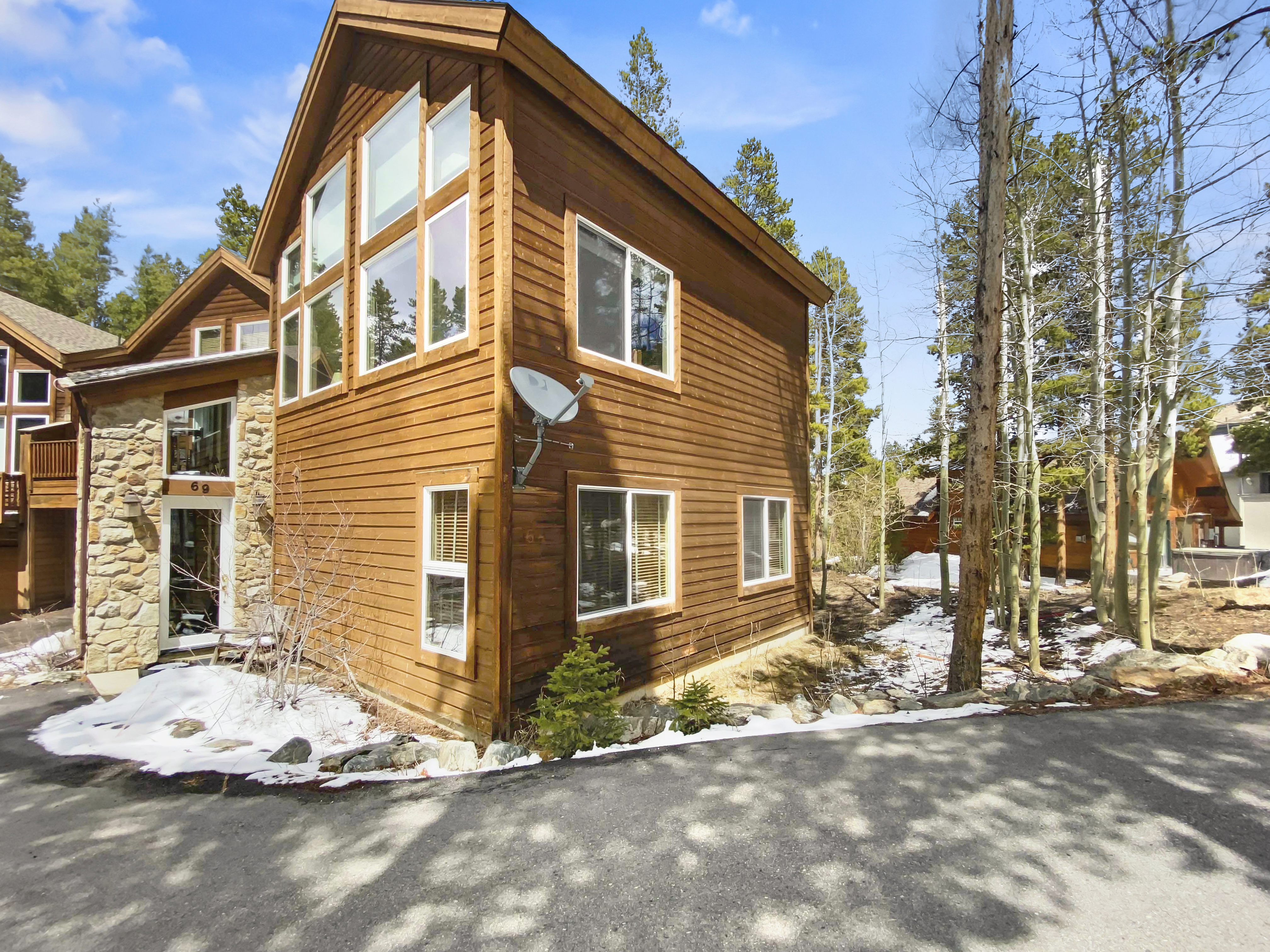 A modern, two-story, wooden house with large windows and a satellite dish, set in a snowy, wooded area.