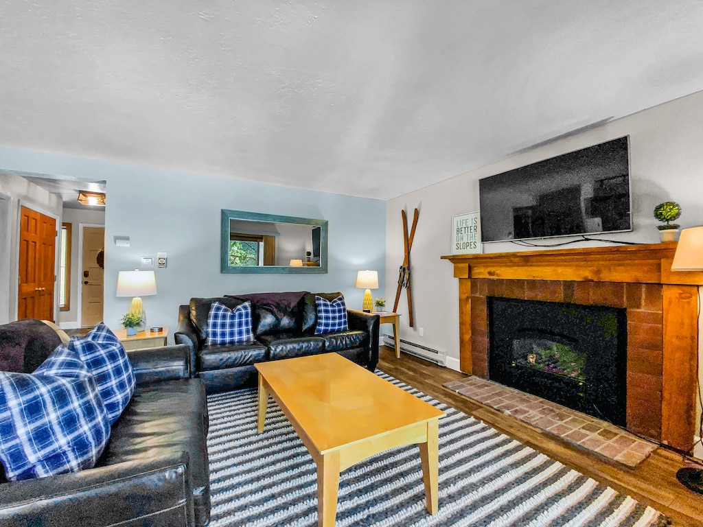 A living room with a striped rug, black leather couches with blue-checkered pillows, a wooden coffee table, a fireplace with a TV mounted above, and wall-mounted skis next to the fireplace.