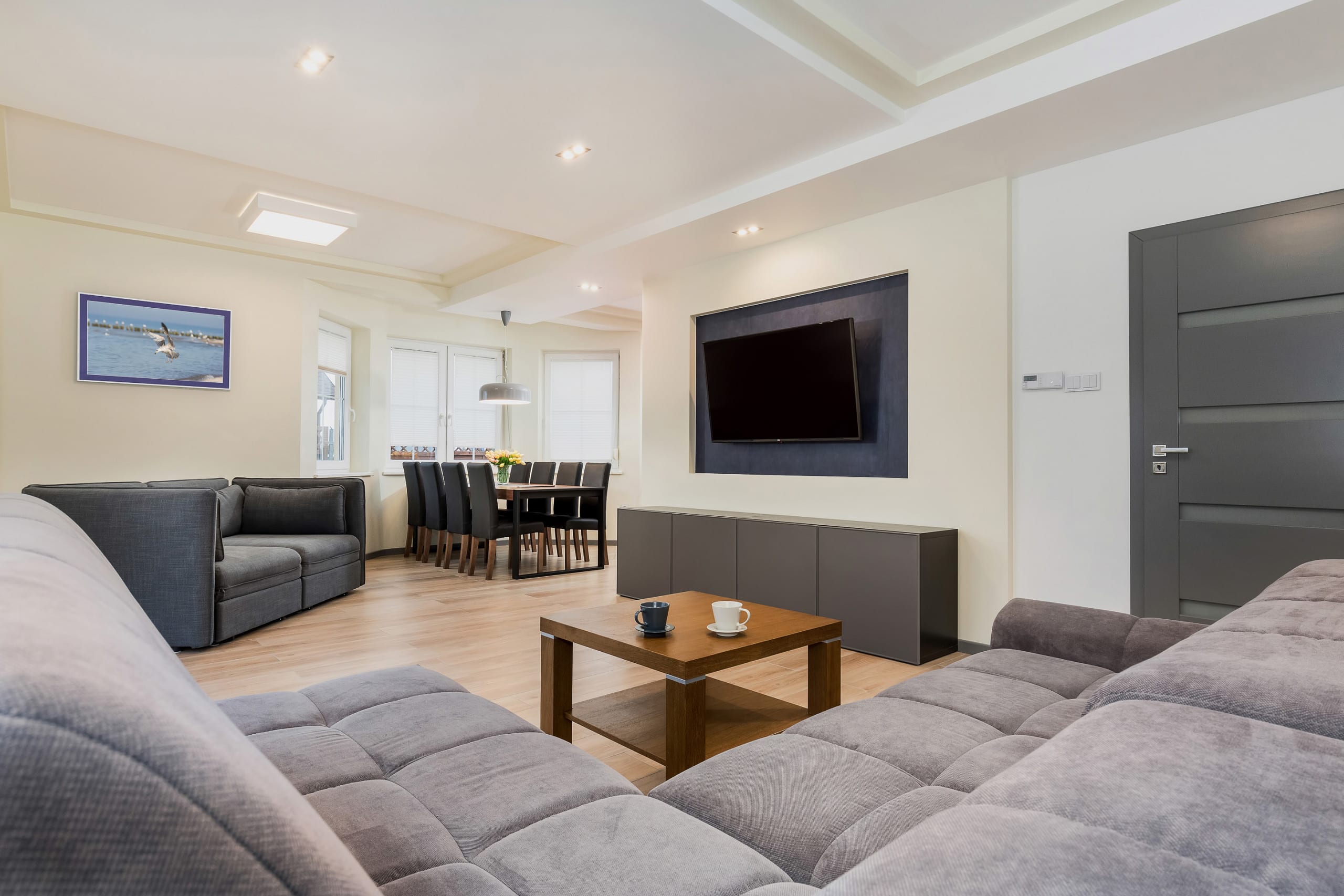 A bright living room featuring a large, neatly made double bed with modern decor and ample natural lighting from a skylight window.