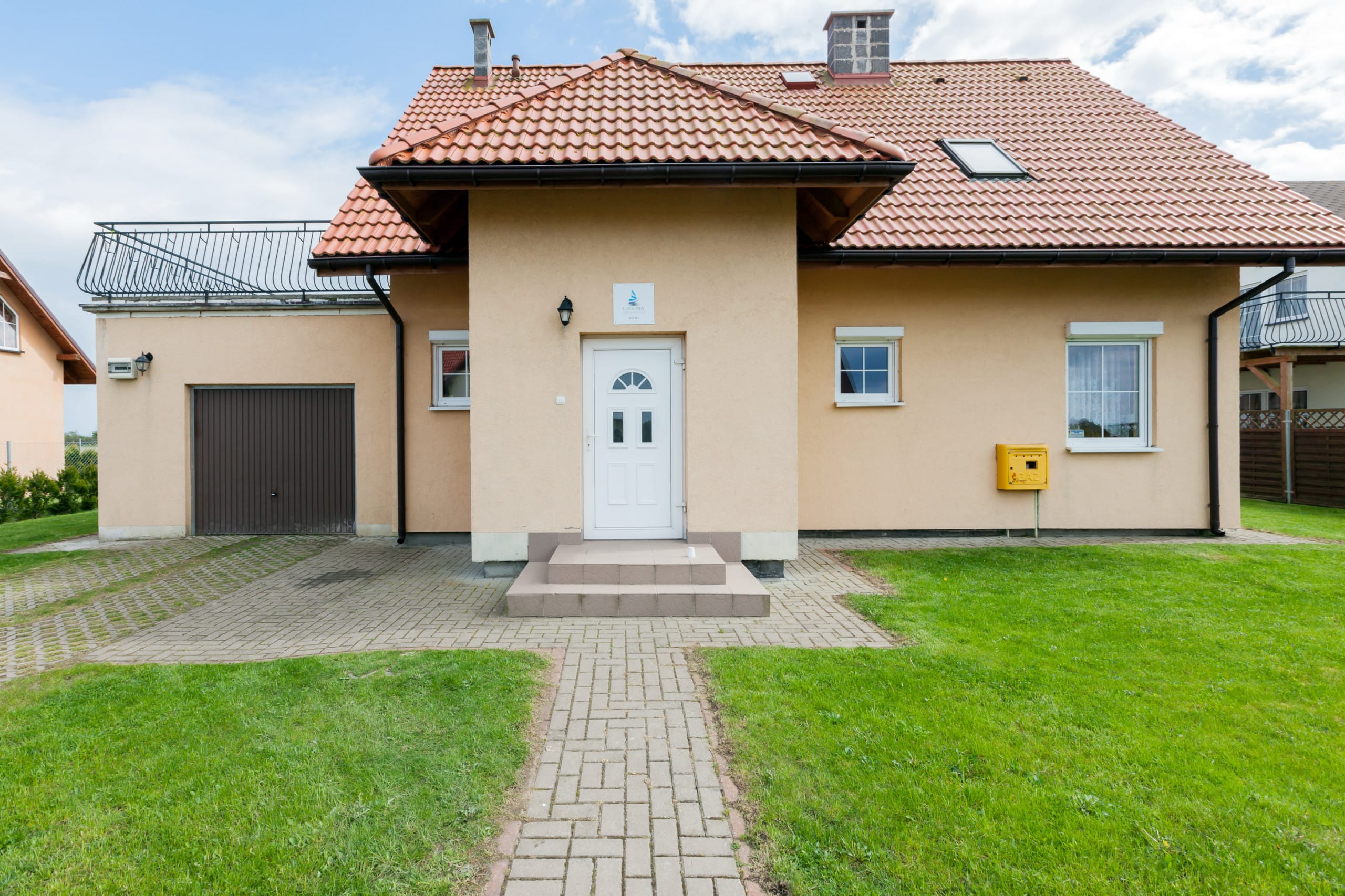 The exterior of a cozy, single-story house with a traditional red roof and a well-maintained lawn leading to the entrance.