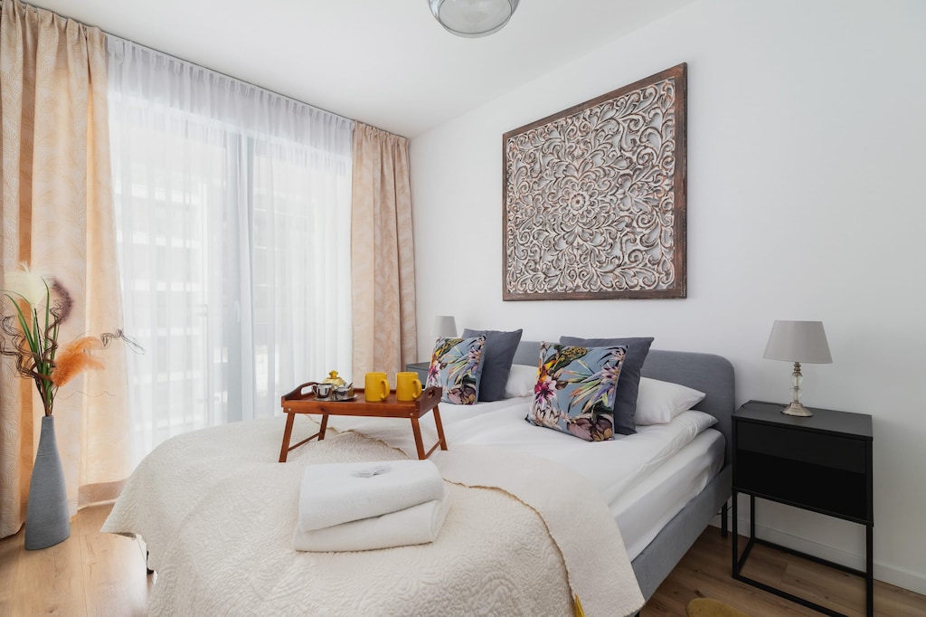 A cozy bedroom featuring a double bed, patterned artwork, and soft natural light.
