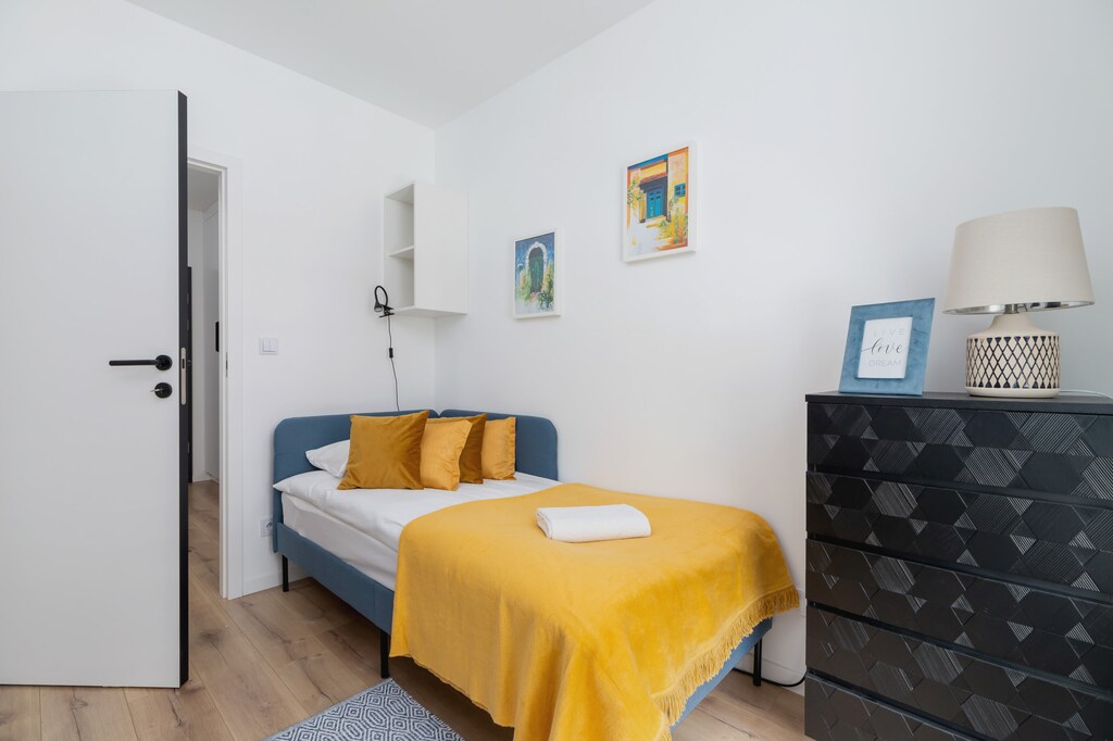 A compact bedroom with a mustard blanket, a bedside table, and minimalist decor.
