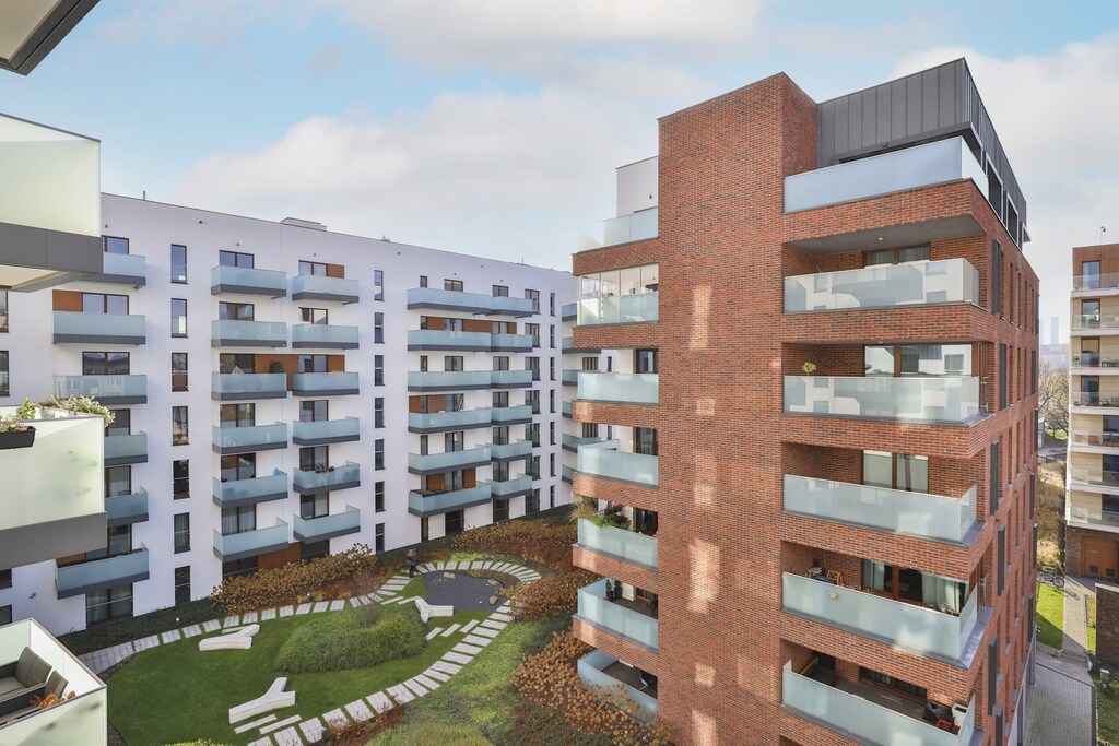 A view of the modern apartment building with a mix of brick and white finishes. A green courtyard adds to the appeal of the property.
