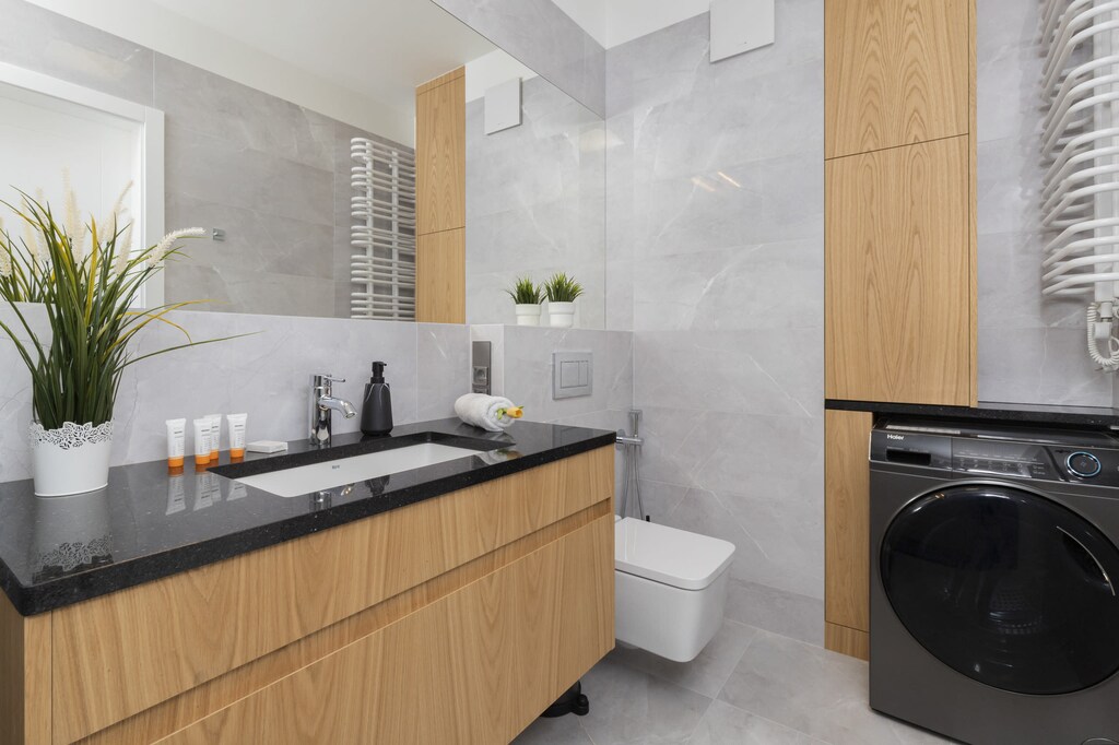 A modern bathroom with wooden cabinets, white tiles, and a washing machine. The design is both functional and stylish.